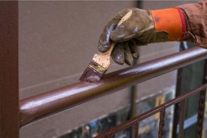 Commercial Painter with gloves on holding a paintbrush while painting a railing.